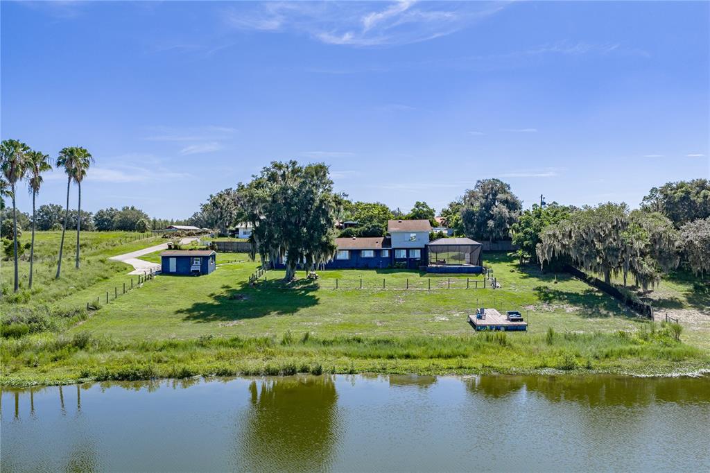 An aerial view shows a blue house with a screened porch overlooking a lake — 2120 HURLEY DRIVE, BARTOW, FL