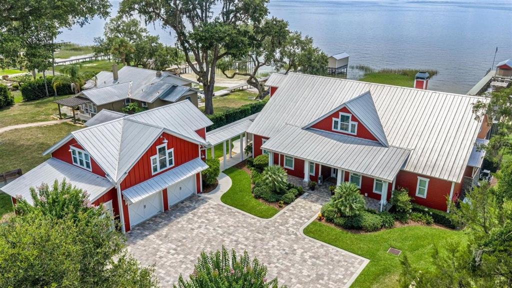 An aerial view of a red farmhouse-style home with a metal roof and paved driveway — 11940 SE 128TH PLACE ROAD, OCKLAWAHA, FL