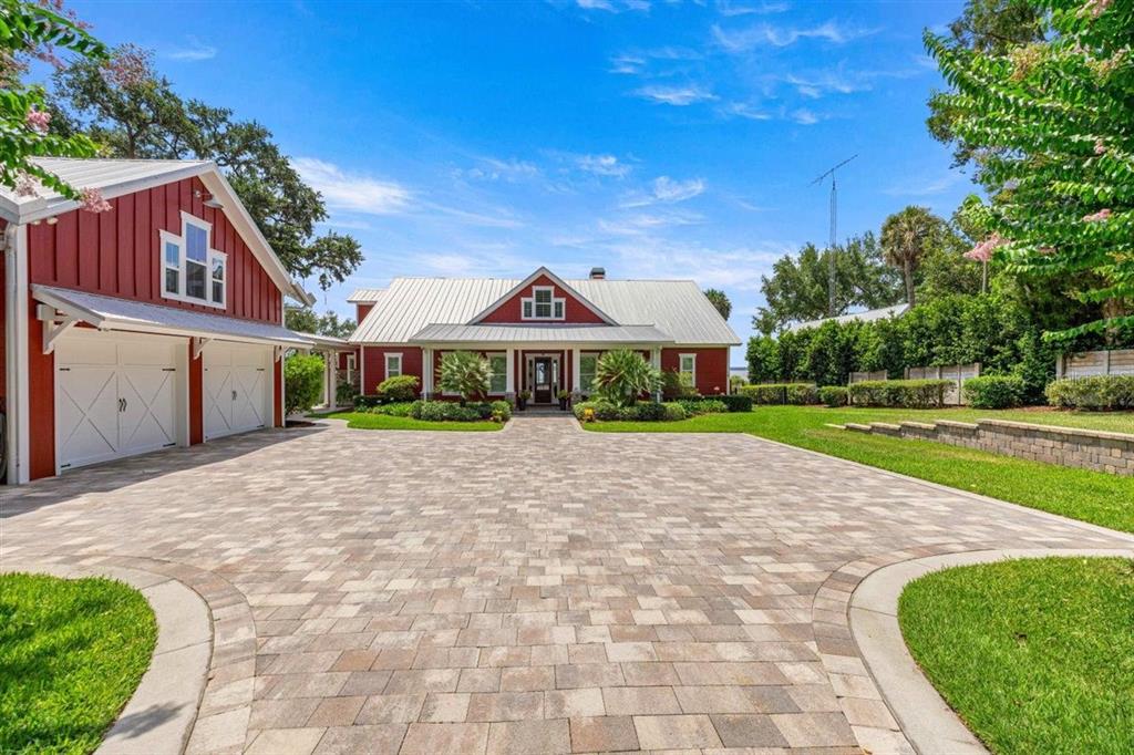 A red house with a metal roof and a large paver driveway under a blue sky — 11940 SE 128TH PLACE ROAD, OCKLAWAHA, FL