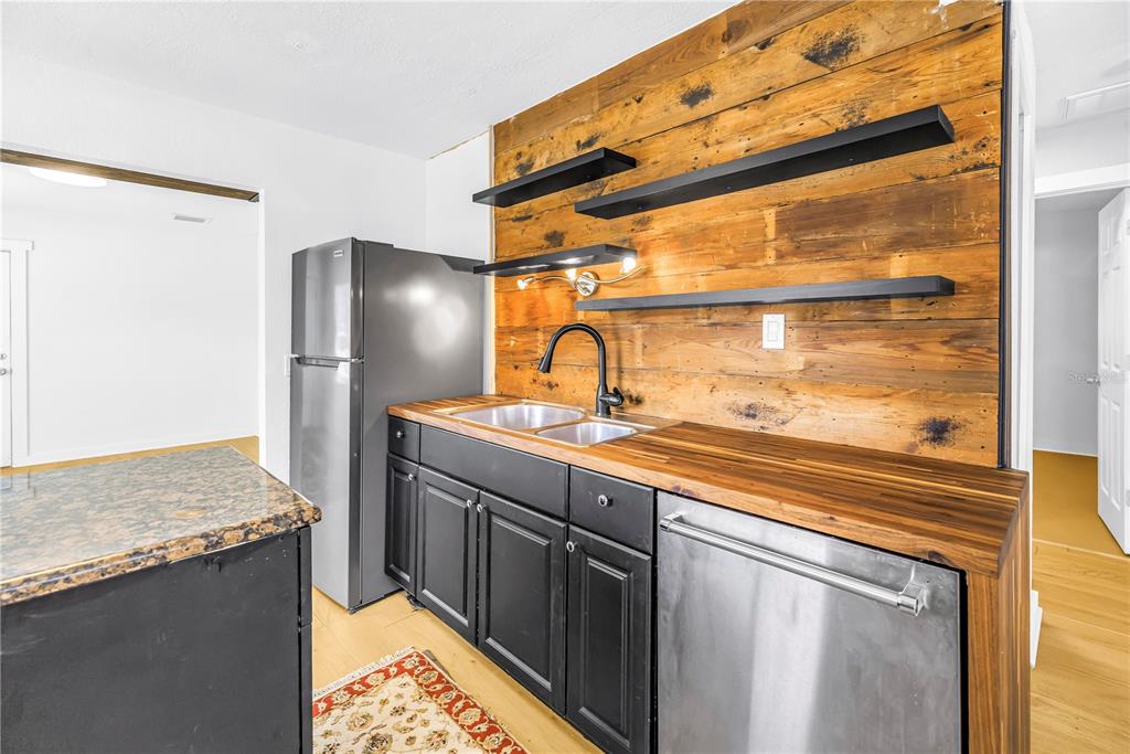 A kitchen features black cabinets, a wood countertop, open shelving, and a rustic wood-plank wall — 2000 27TH AVENUE N, ST PETERSBURG, FL