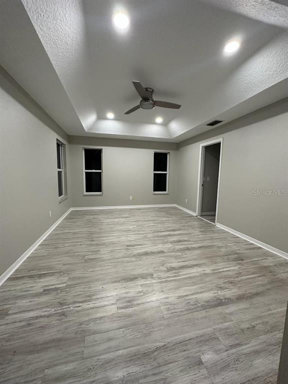 A bedroom with gray walls, wood-look flooring, and a tray ceiling with a fan — 4743 CHALFONT DRIVE, ORLANDO, FL