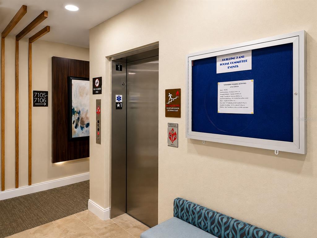 An elevator lobby features a stainless steel elevator, a blue bulletin board, and a bench — 7545 LAUREATE BOULEVARD UNIT 7301, ORLANDO, FL