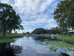 A view of a canal with boat docks, surrounding trees, and a cloudy blue sky — 153 FERN DRIVE, DEBARY, FL