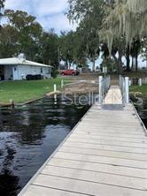 A wooden dock extends into a body of water toward a grassy yard and house — 153 FERN DRIVE, DEBARY, FL