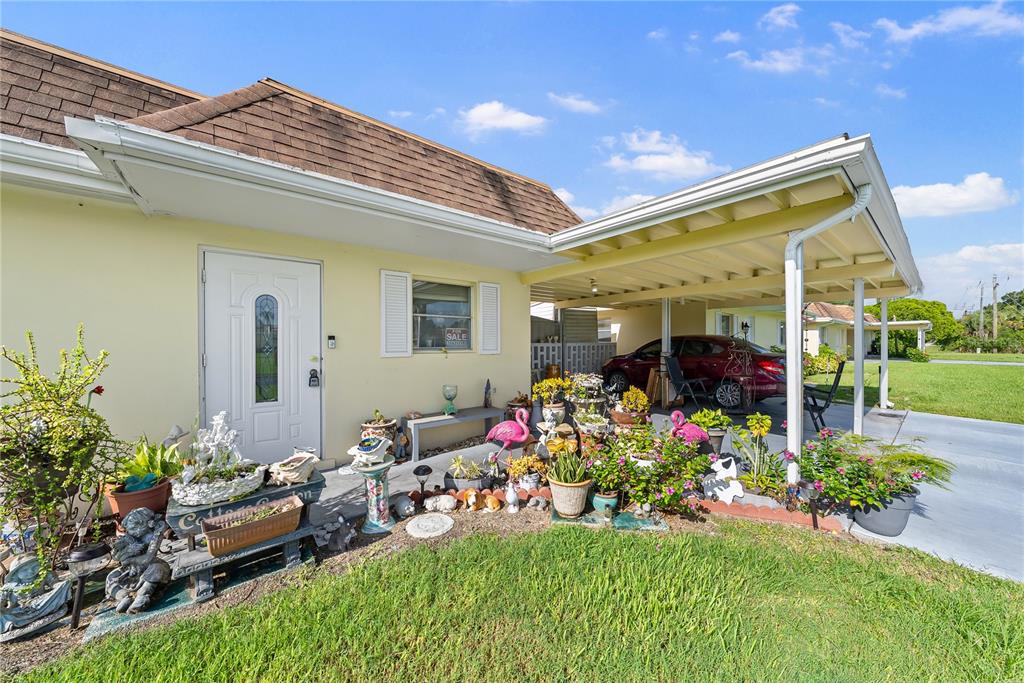 A single-story house exterior features a white front door, a carport, and a landscaped garden — 2208 GARDENIA WAY, LEHIGH ACRES, FL