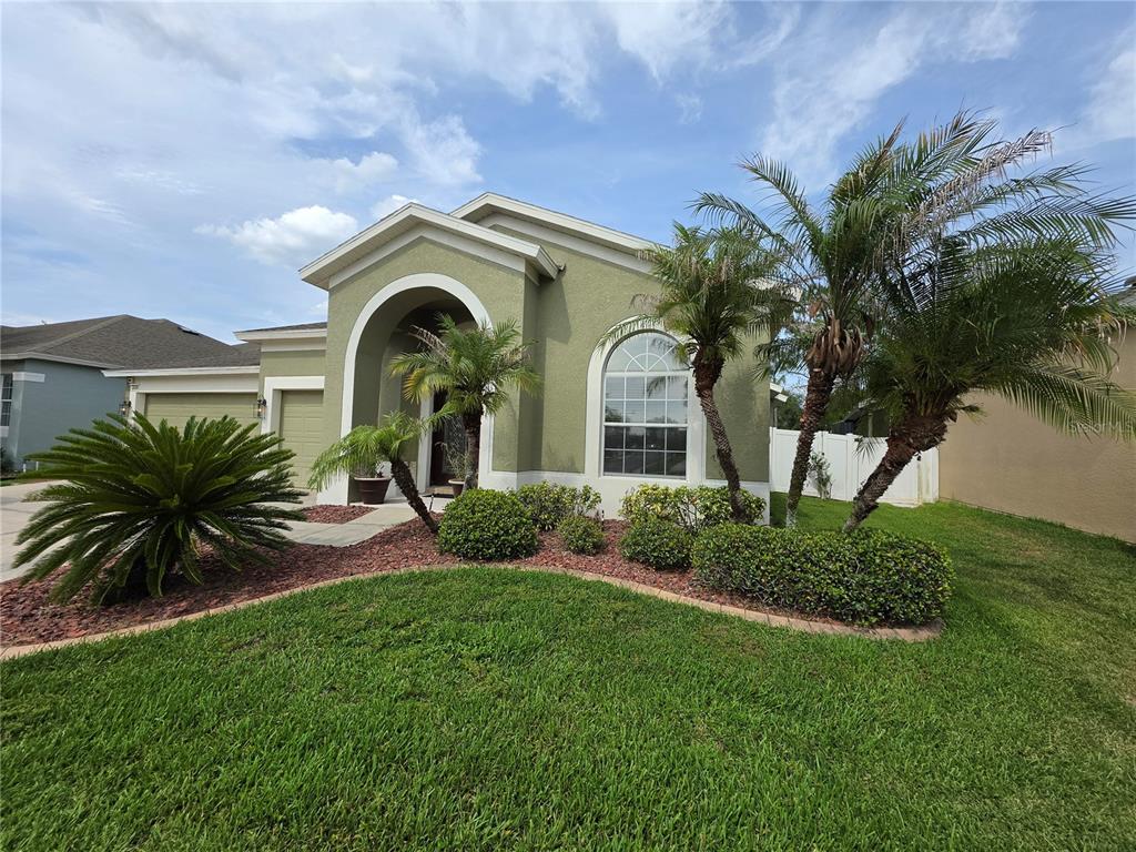 A single-story house with a three-car garage, arched entryway, and a landscaped front yard — 3608 JUNEBERRY DRIVE, WESLEY CHAPEL, FL