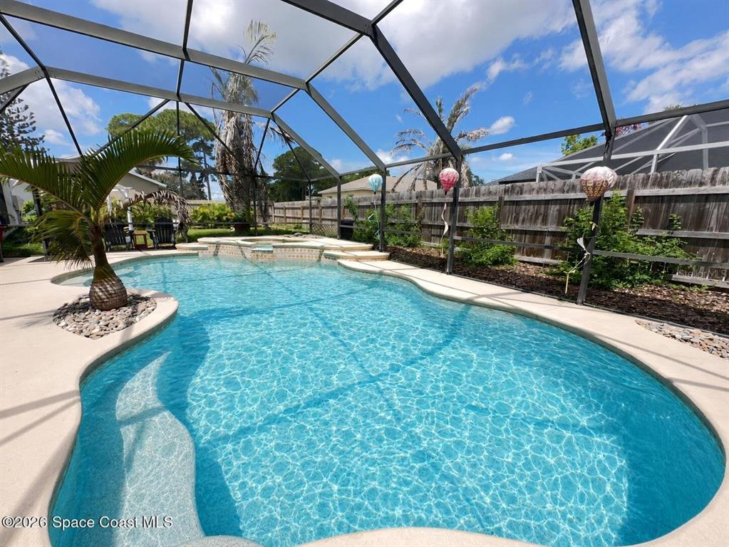 A screened-in swimming pool with a spa and palm tree sits in a fenced backyard — 130 COUNTRY WOODS PLACE, MERRITT ISLAND, FL