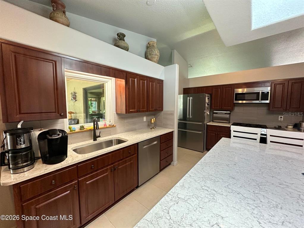 A kitchen features dark wood cabinets, light countertops, stainless steel appliances, and a large island — 130 COUNTRY WOODS PLACE, MERRITT ISLAND, FL