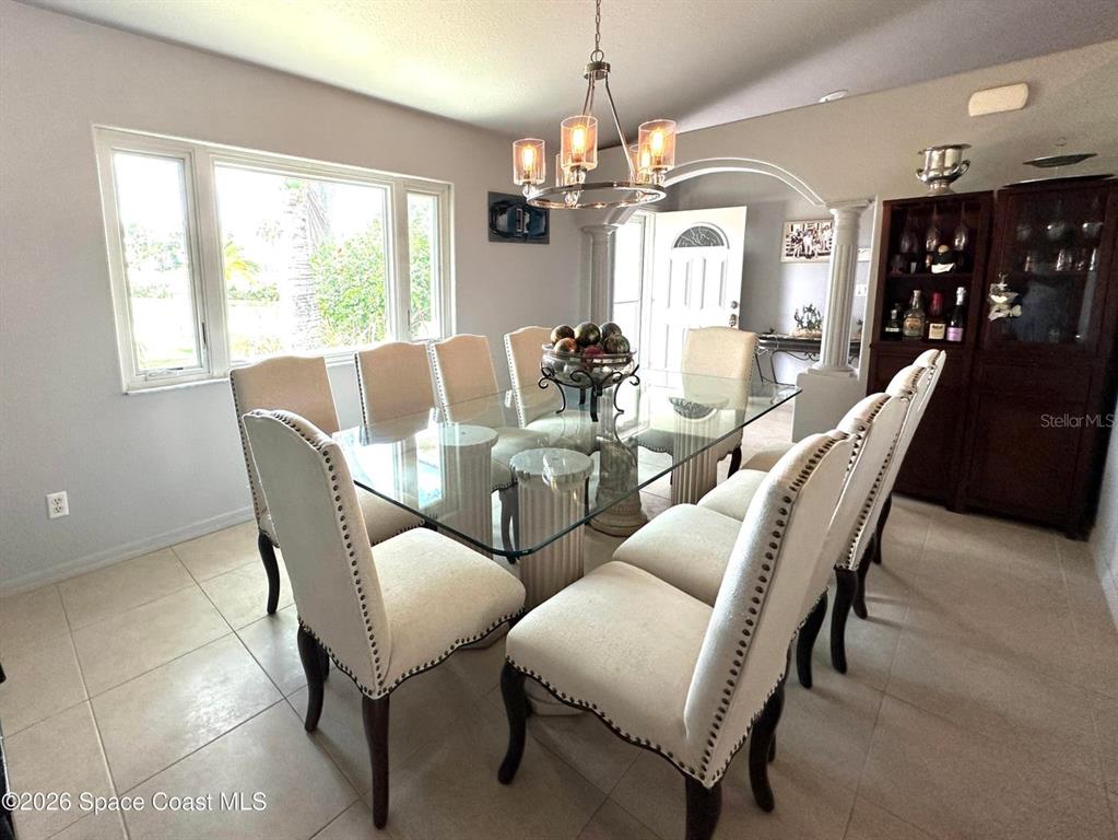 A dining room features a glass-topped table with upholstered chairs under a modern chandelier — 130 COUNTRY WOODS PLACE, MERRITT ISLAND, FL