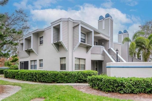A multi-story apartment building with light gray siding and a low hedge in the foreground — 8737 BARDMOOR PLACE UNIT 101, SEMINOLE, FL