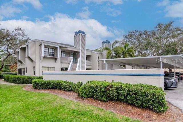 A multi-story apartment building features beige siding, a covered carport, and a manicured hedge — 8737 BARDMOOR PLACE UNIT 101, SEMINOLE, FL