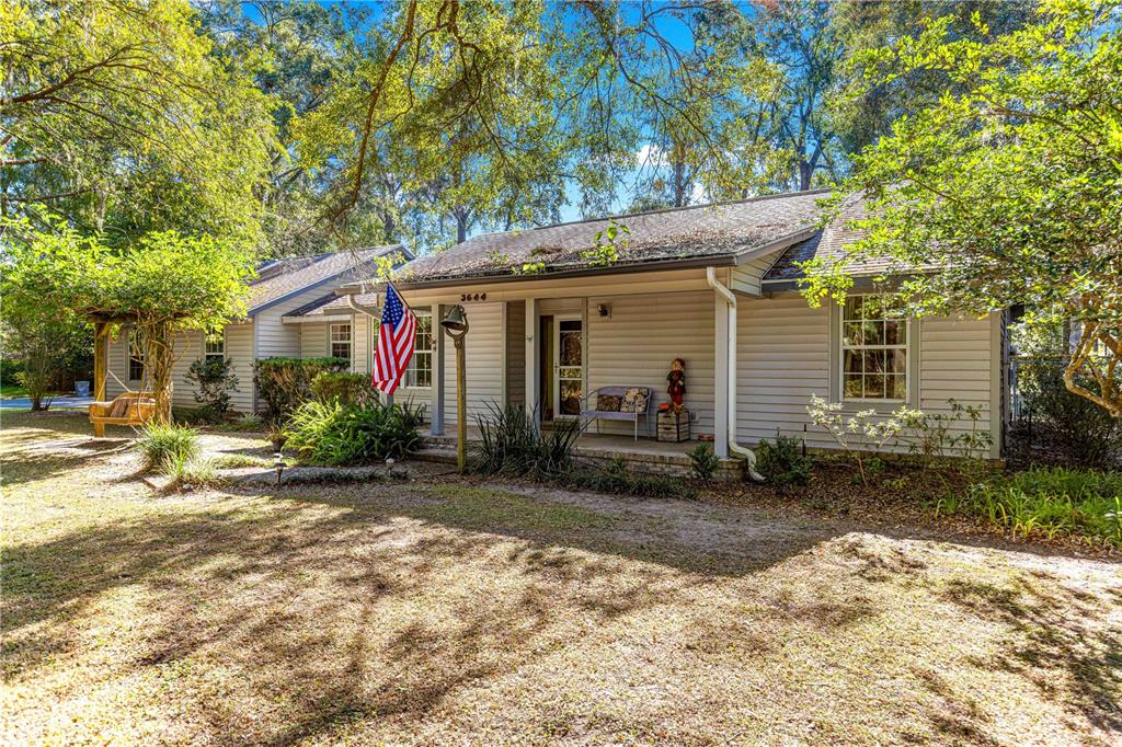 A covered front porch features a light-colored siding, a metal bench, and an American flag — 3644 SE 22ND AVENUE, OCALA, FL