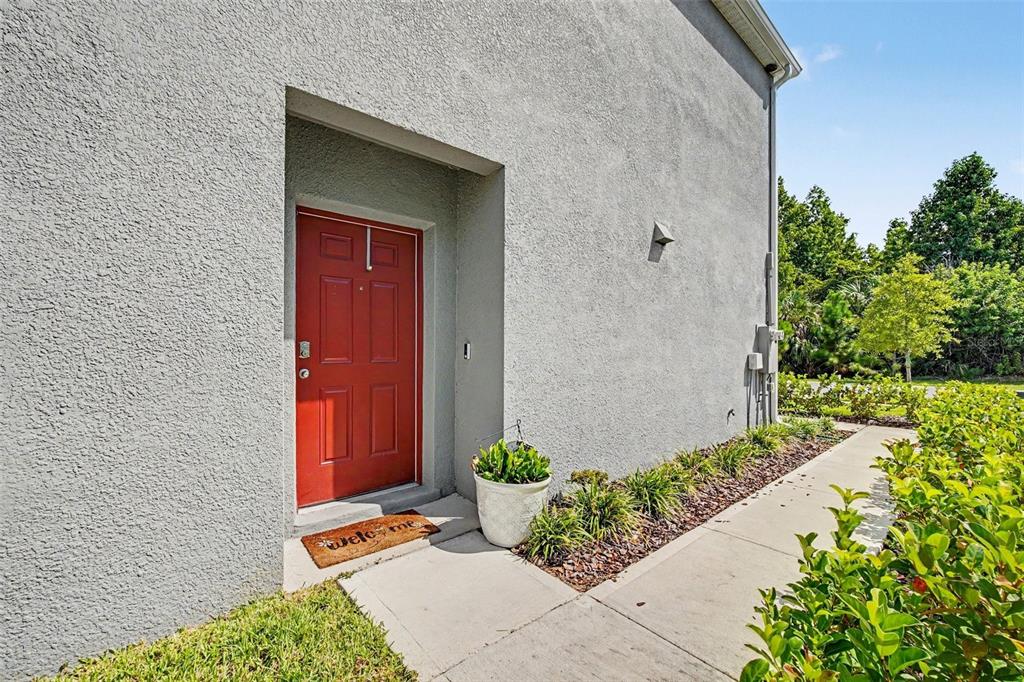 A red front door is set into the gray stucco exterior of a house — 2126 GENTLE RAIN DRIVE, EDGEWATER, FL