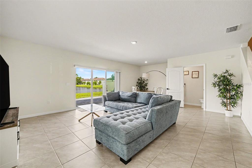 A living room with tile floors, a gray sectional sofa, and sliding doors overlooking a pond — 2126 GENTLE RAIN DRIVE, EDGEWATER, FL