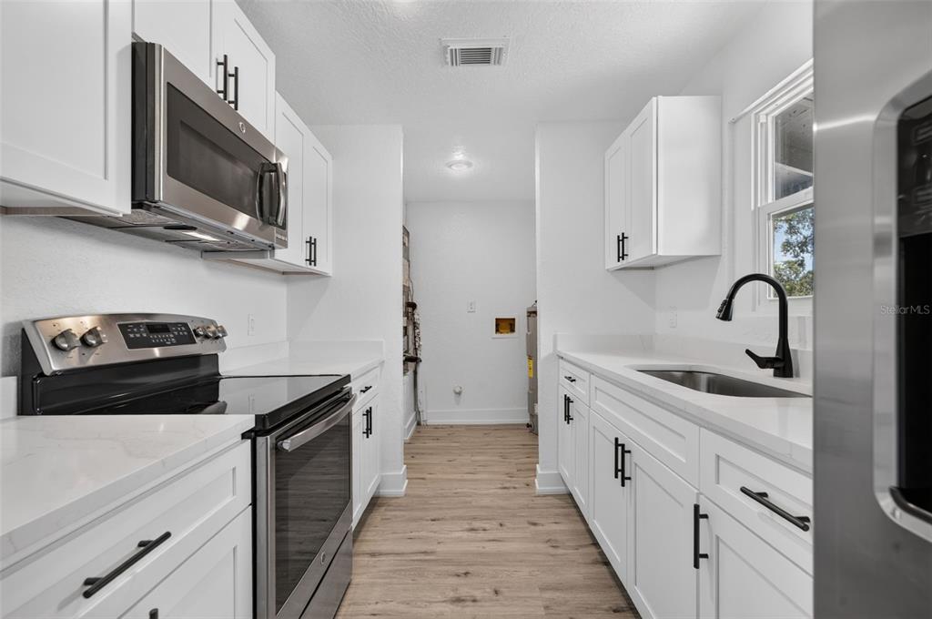A galley kitchen features white cabinets, stainless steel appliances, and light wood-look flooring — 1911 WATER STREET, SANFORD, FL