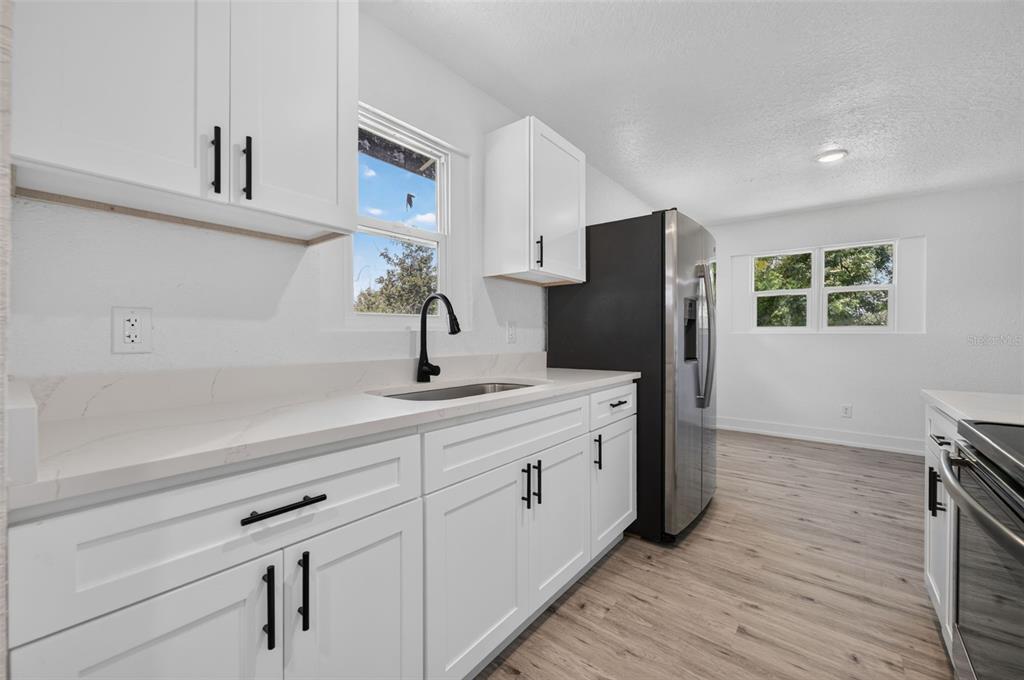 A kitchen features white shaker cabinets, quartz countertops, stainless steel appliances, and light wood flooring — 1911 WATER STREET, SANFORD, FL