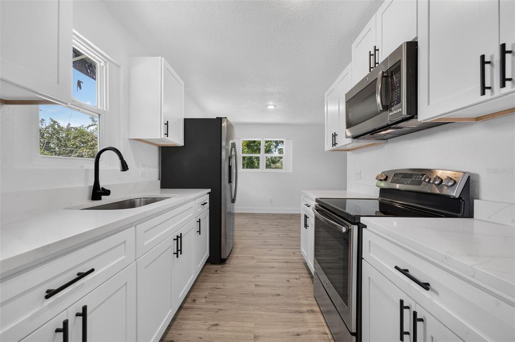 A galley kitchen features white cabinets, black hardware, stainless steel appliances, and light wood flooring — 1911 WATER STREET, SANFORD, FL
