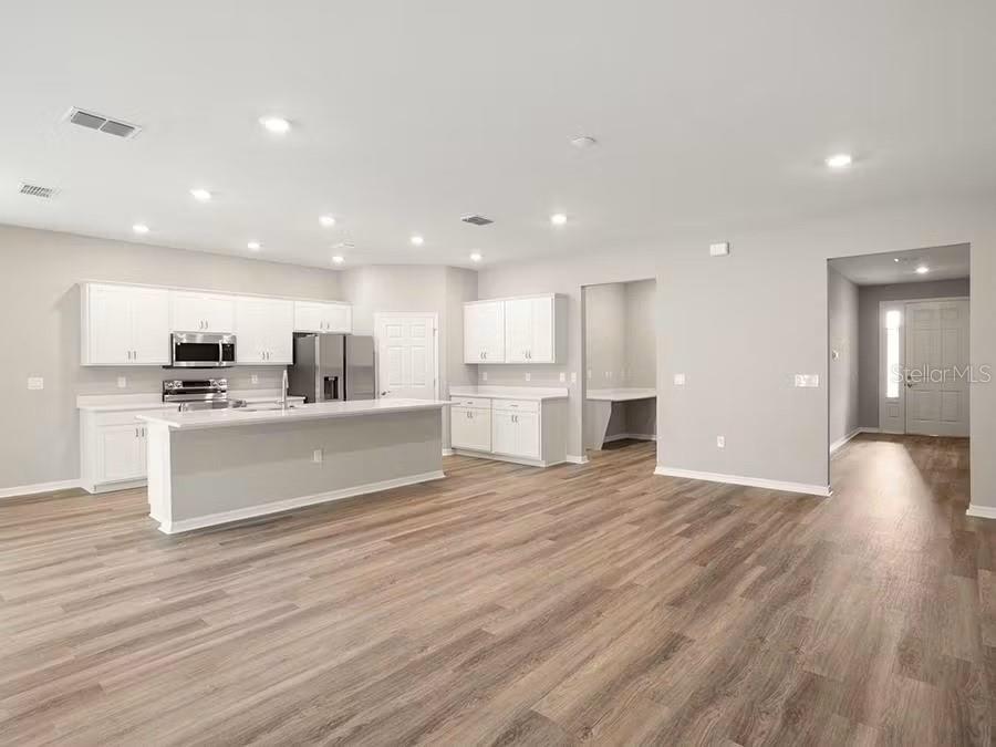 A modern kitchen with white cabinets, a central island, and wood-look flooring in an open space — 7636 SW 6TH LOOP, OCALA, FL