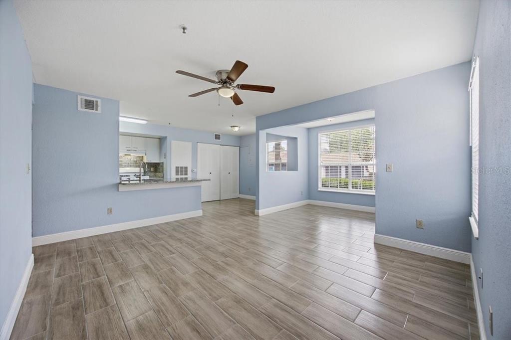 An open-concept living area with light blue walls, wood-look tile flooring, and a kitchen pass-through — 1612 COLUMBIA ARMS CIRCLE UNIT 137, KISSIMMEE, FL