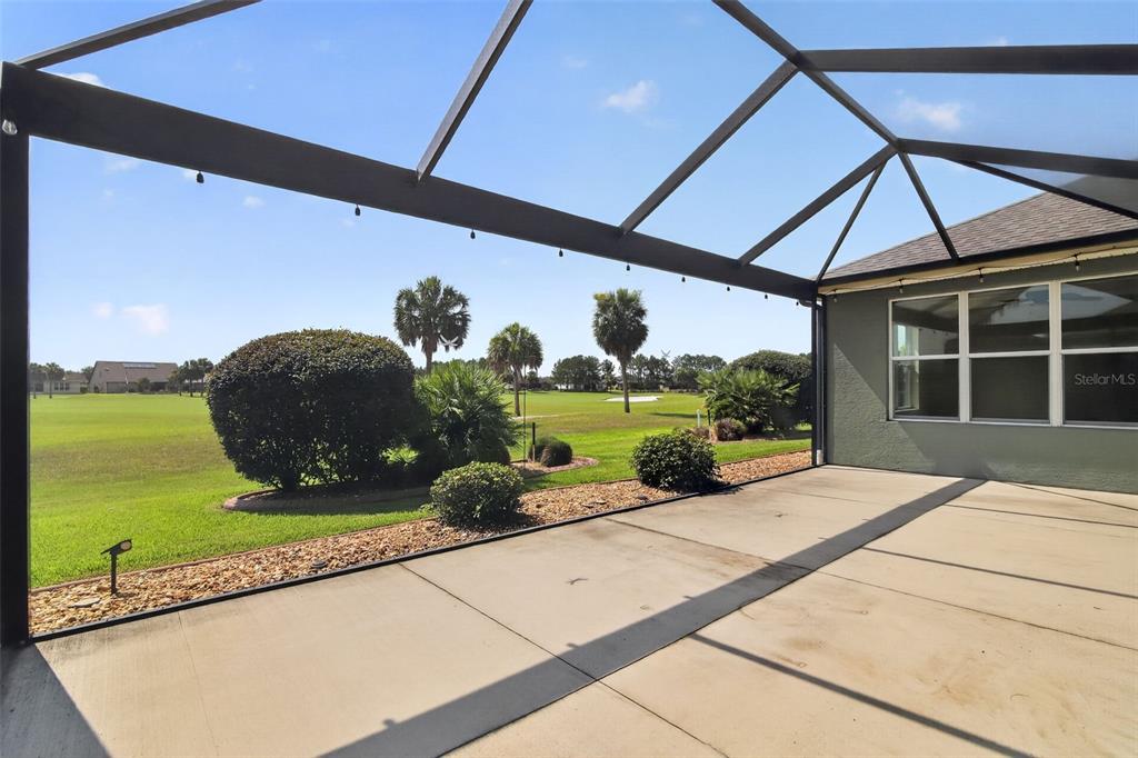 A screened-in concrete patio overlooks a grassy golf course with palm trees and landscaping — 9439 SW 71ST LOOP, OCALA, FL