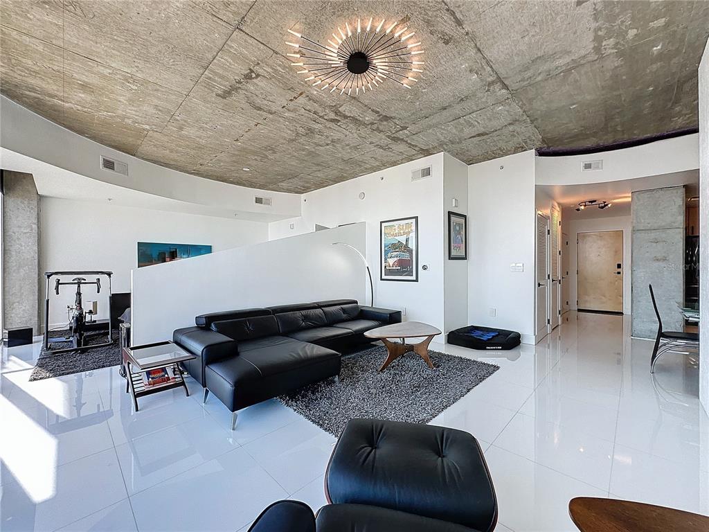 A modern living room features a concrete ceiling, white tile floors, and a black sectional sofa — 155 S COURT AVENUE UNIT 2111, ORLANDO, FL