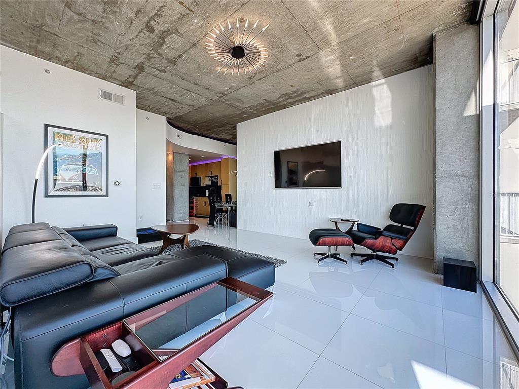 A modern living room features a concrete ceiling, white tile floors, and a black leather sofa — 155 S COURT AVENUE UNIT 2111, ORLANDO, FL