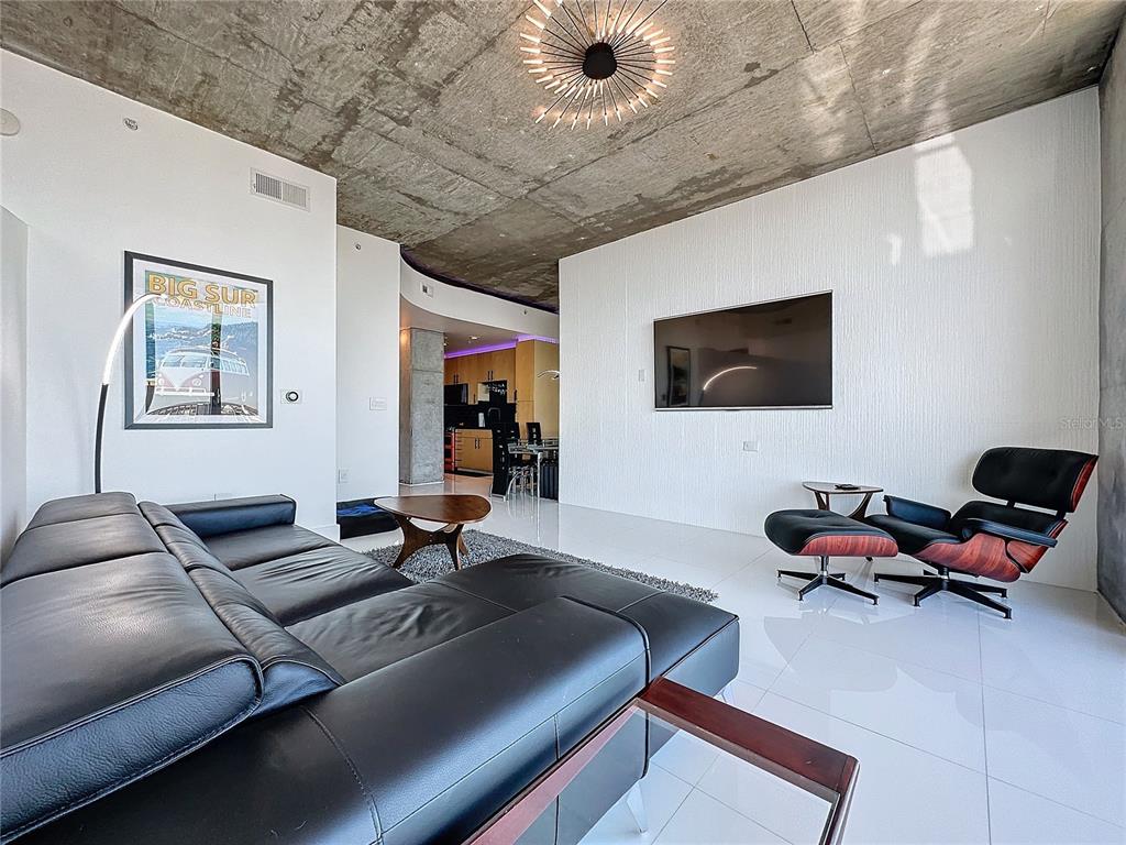 A modern living room features a concrete ceiling, white tile floors, and a black leather sofa — 155 S COURT AVENUE UNIT 2111, ORLANDO, FL