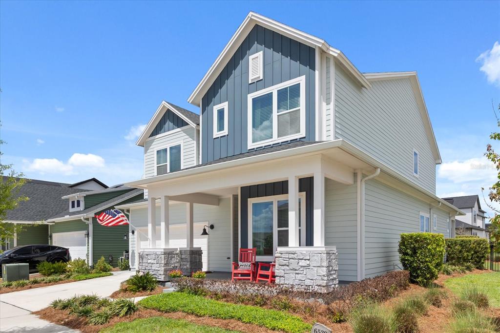 A two-story house with blue and light gray siding, a stone-accented porch, and red chairs — 6539 QUEST STREET, ST CLOUD, FL