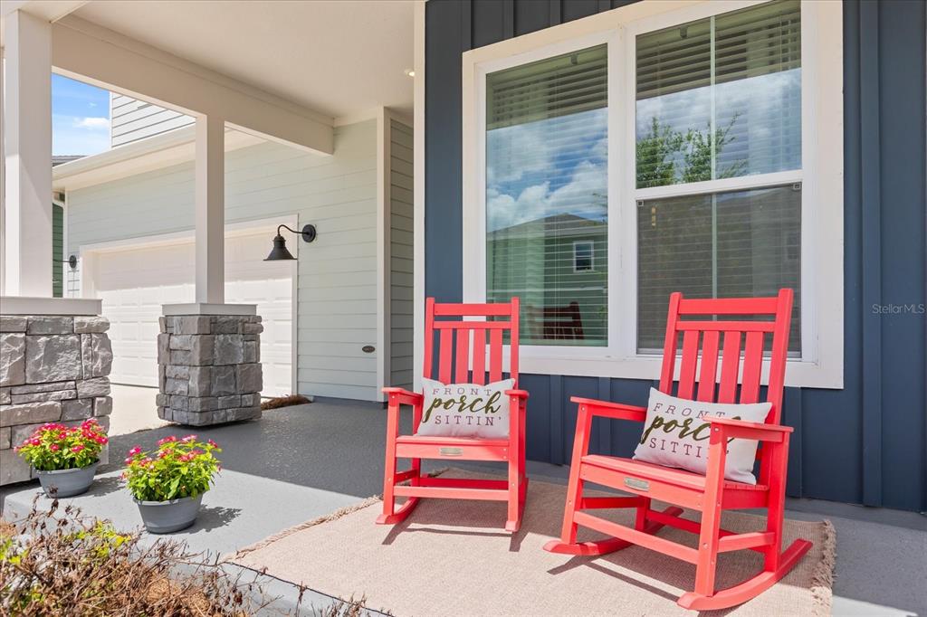 Two bright red rocking chairs with decorative pillows sit on a covered front porch — 6539 QUEST STREET, ST CLOUD, FL