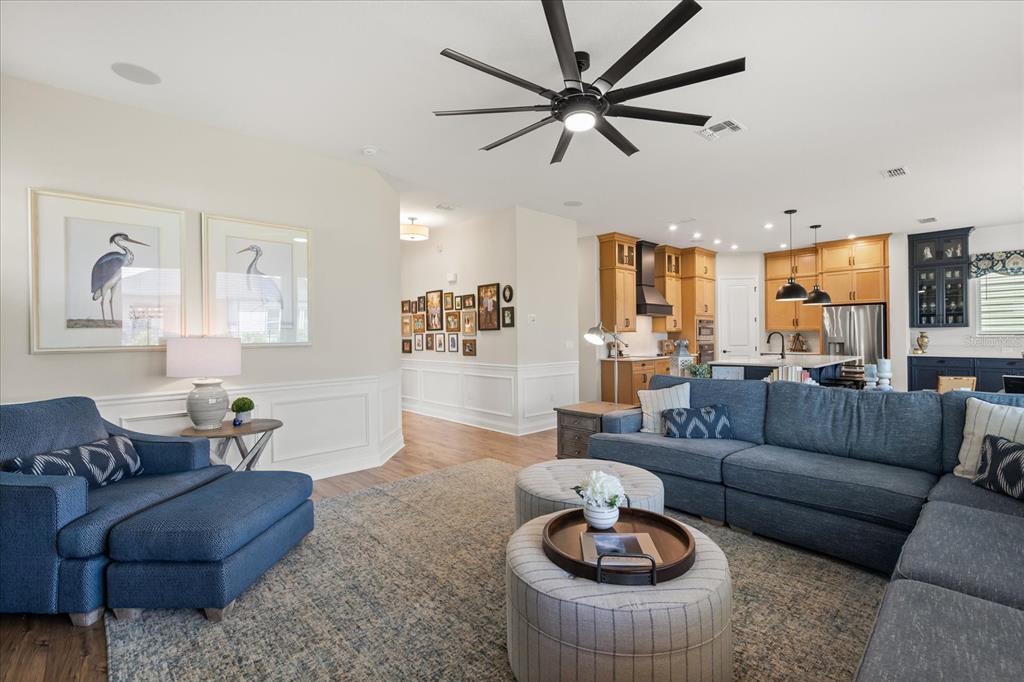 A living room with a blue sectional, two round ottomans, and an open-concept kitchen — 6539 QUEST STREET, ST CLOUD, FL