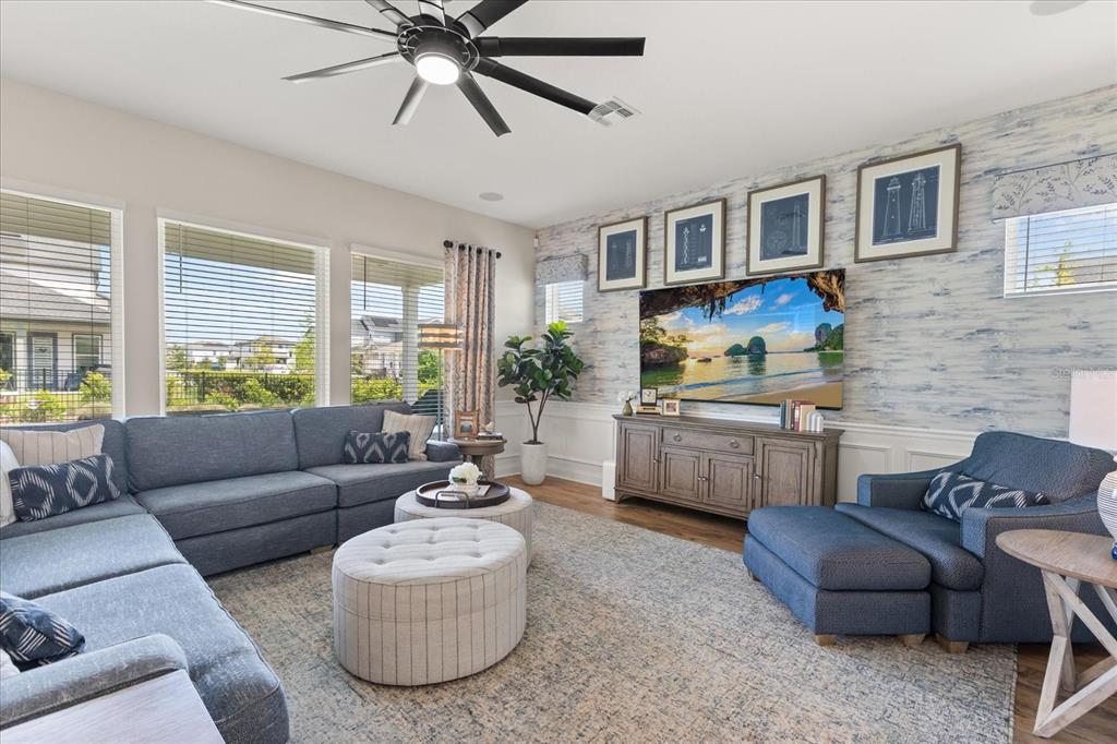 A living room features a blue sectional sofa, a television, and a patterned accent wall — 6539 QUEST STREET, ST CLOUD, FL