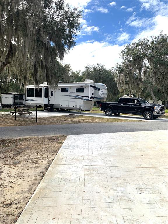 A black pickup truck is parked next to a large white fifth-wheel RV outdoors — 15991 NE 243RD PLACE ROAD UNIT 54, FORT MC COY, FL