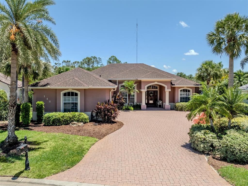 A single-story stucco house with a paved driveway and palm trees under a blue sky — 148 WADING BIRD DRIVE, VENICE, FL