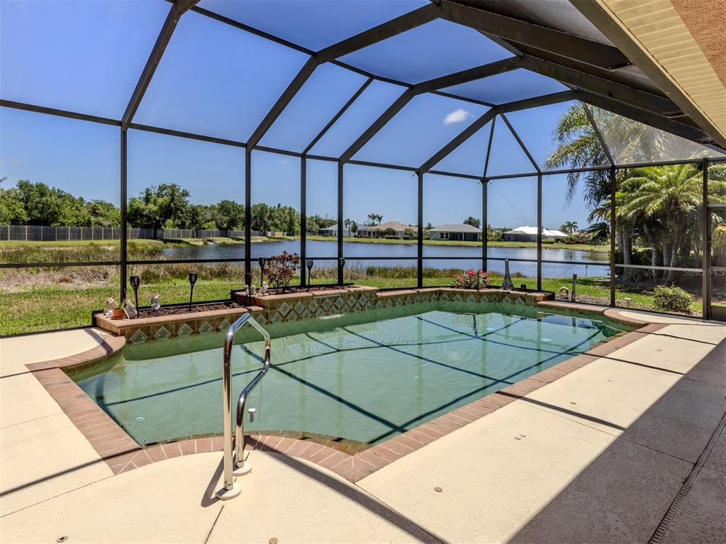 A screened-in swimming pool with a raised tiled spillway overlooks a lake and grassy yard — 148 WADING BIRD DRIVE, VENICE, FL