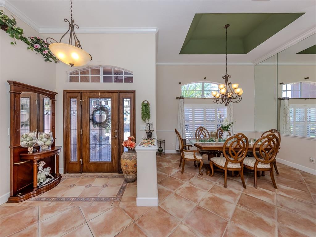 A dining room and entryway feature tile floors, a wooden front door, and chandeliers — 148 WADING BIRD DRIVE, VENICE, FL