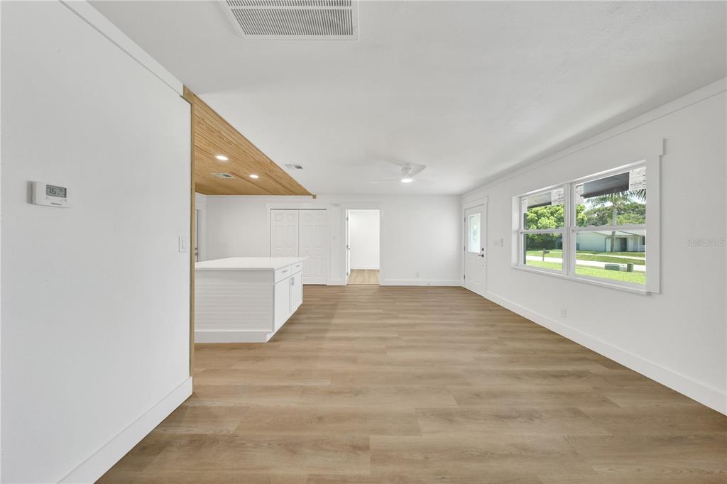 A bright, open-concept living area features light wood-look flooring, white walls, and a wooden ceiling — 2264 WINCHESTER DRIVE, DUNEDIN, FL