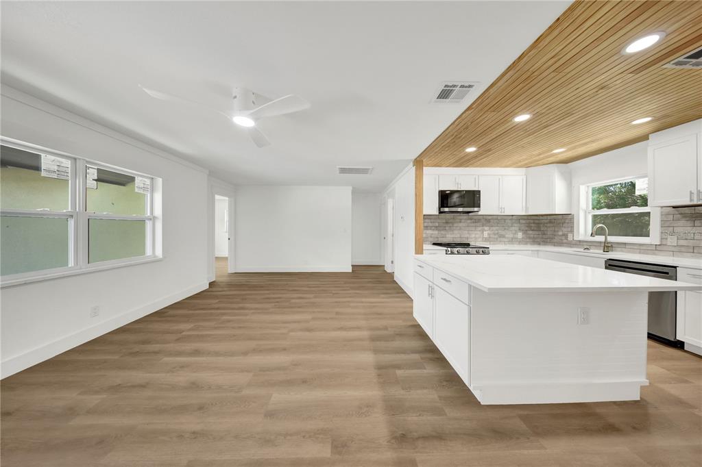 An open-concept kitchen and living area featuring wood-plank ceilings, white cabinetry, and light wood flooring — 2264 WINCHESTER DRIVE, DUNEDIN, FL