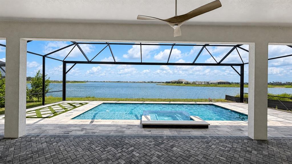 A rectangular swimming pool with an integrated spa overlooks a large lake under a cloudy sky — 812 BLUE SHELL LOOP, SARASOTA, FL
