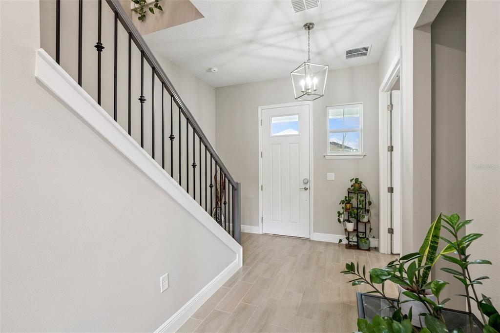 A bright entryway features light wood-look tile flooring, a staircase with black railings, and a chandelier — 6236 TRAILBLAZE BEND, ST CLOUD, FL