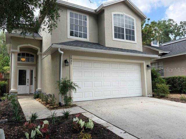 A two-story suburban house features a beige stucco exterior, a two-car garage, and landscaping — 1931 LOST SPRING COURT, LONGWOOD, FL