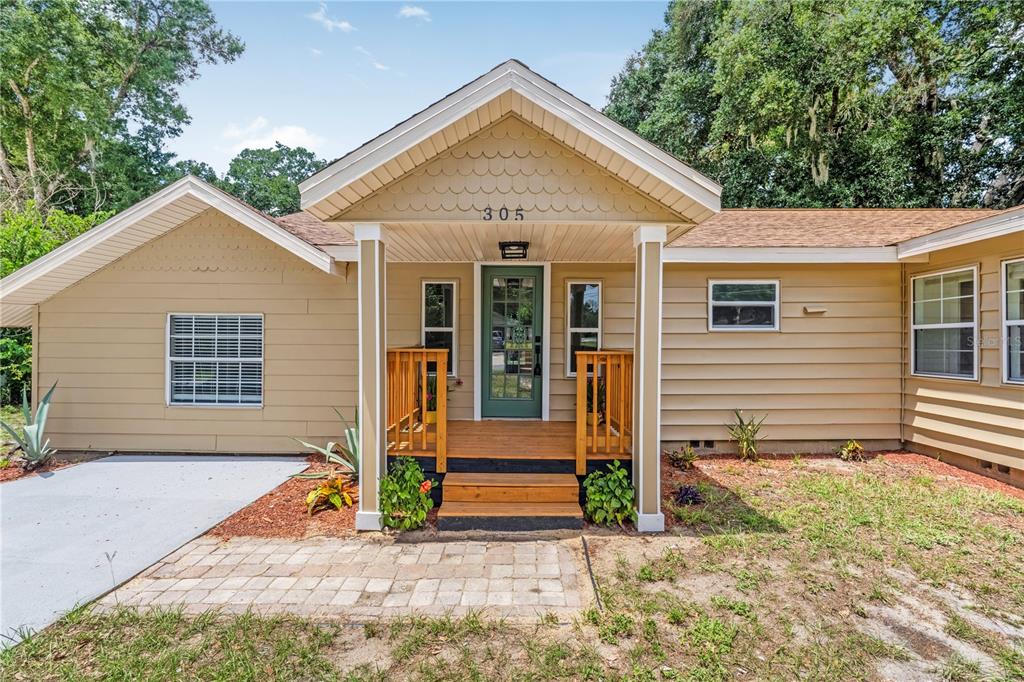 A tan house exterior features a front porch with wooden steps and a green door — 305 S ROSSITER STREET, MOUNT DORA, FL