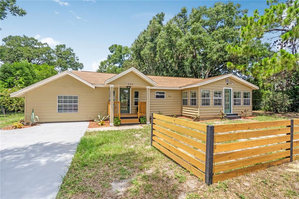 A single-story house with tan siding, a brown roof, and a wooden horizontal slat fence — 305 S ROSSITER STREET, MOUNT DORA, FL