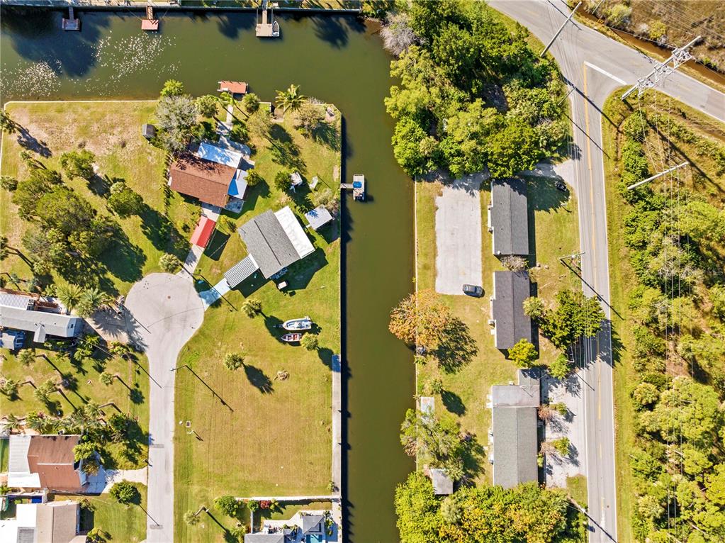 An aerial view shows a canal separating residential properties and a road with power lines — 0 SHEEPSHEAD DRIVE, HUDSON, FL