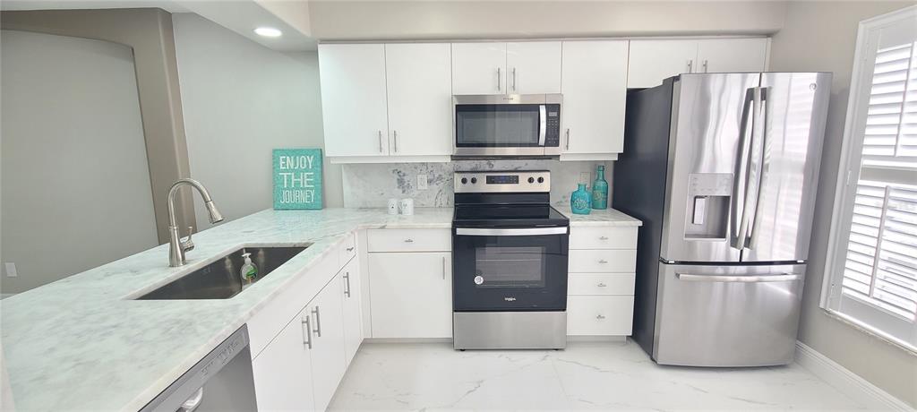 A modern kitchen features white cabinets, stainless steel appliances, and marble-look countertops and flooring — 3531 FOREST BRANCH DRIVE UNIT D, PORT ORANGE, FL