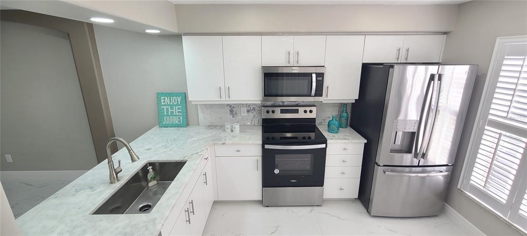 A kitchen features white cabinets, stainless steel appliances, and a marble-patterned countertop with a sink — 3531 FOREST BRANCH DRIVE UNIT D, PORT ORANGE, FL