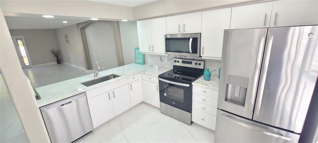 A modern kitchen features white cabinets, stainless steel appliances, and marble-look countertops and flooring — 3531 FOREST BRANCH DRIVE UNIT D, PORT ORANGE, FL