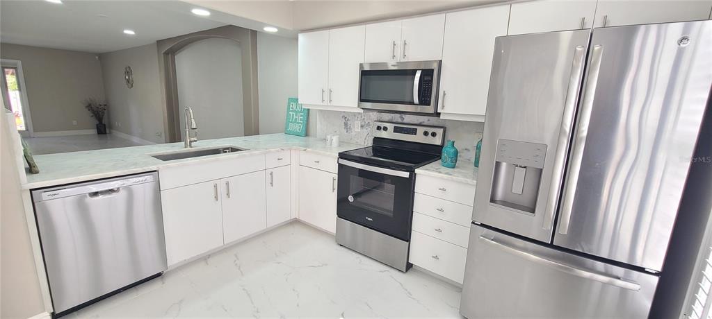 A modern kitchen features white cabinets, stainless steel appliances, and marble-look countertops and flooring — 3531 FOREST BRANCH DRIVE UNIT D, PORT ORANGE, FL
