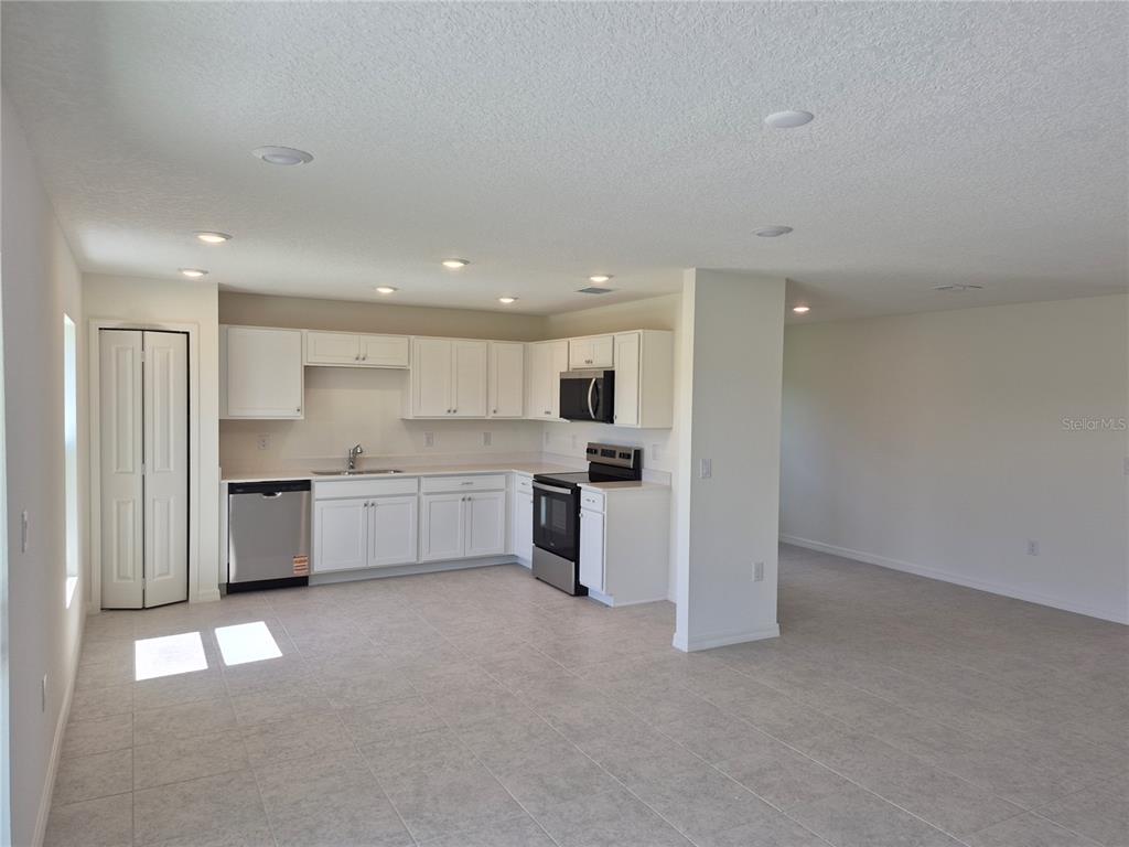 A kitchen with white cabinets and a dishwasher sits adjacent to an open living area — 8810 PINE BARK WAY, WILDWOOD, FL