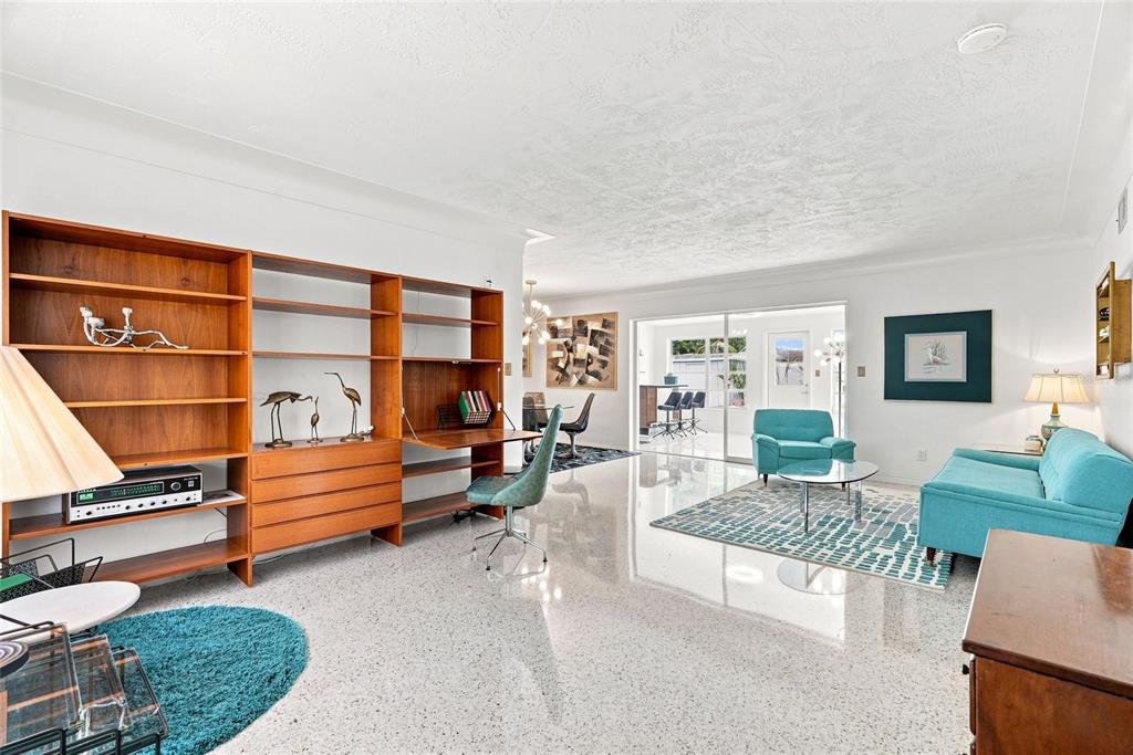 A bright living room features a large wooden wall unit, teal furniture, and terrazzo flooring — 1842 59TH WAY N, ST PETERSBURG, FL