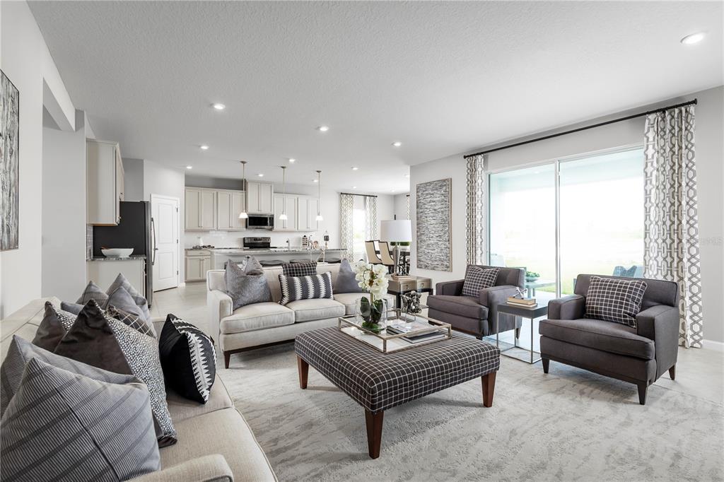 A bright, open-concept living room features neutral furniture, a large ottoman, and an adjacent kitchen — 11062 NELLIE CROSSING CIRCLE, CLERMONT, FL